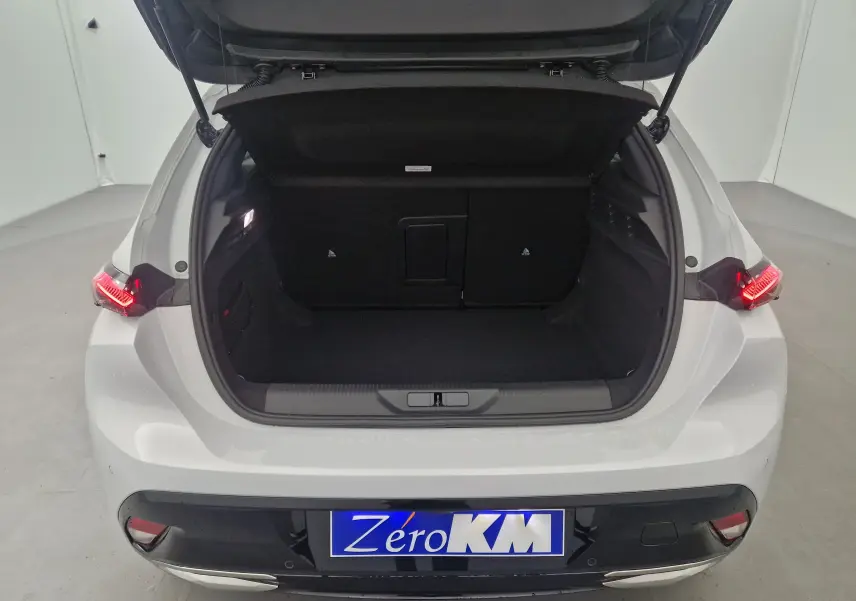Coffre ouvert vu de l'arrière d'une Peugeot 308 blanche Okenite 2025 avec feux arrière allumés et plaque Zero KM.