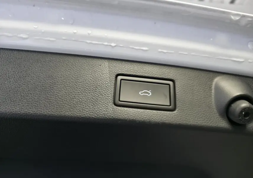 Gros plan sur le bouton de déverrouillage électrique du hayon, entouré de plastique noir, sur Volkswagen Arteon blanc.