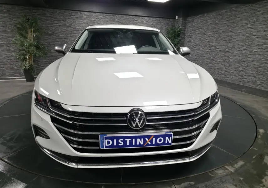 Vue avant d'une Volkswagen Arteon blanche avec calandre horizontale noire et logo VW centré dans un showroom.