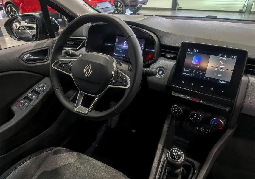 Vue intérieure côté conducteur de la Renault Clio V 2025 avec volant multifonction, écran tactile et levier de vitesse manuel.