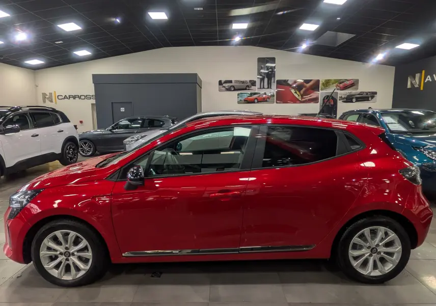 Profil côté gauche d'une Renault Clio V Rouge Flamme en intérieur, soulignant ses lignes dynamiques et jantes alliage.