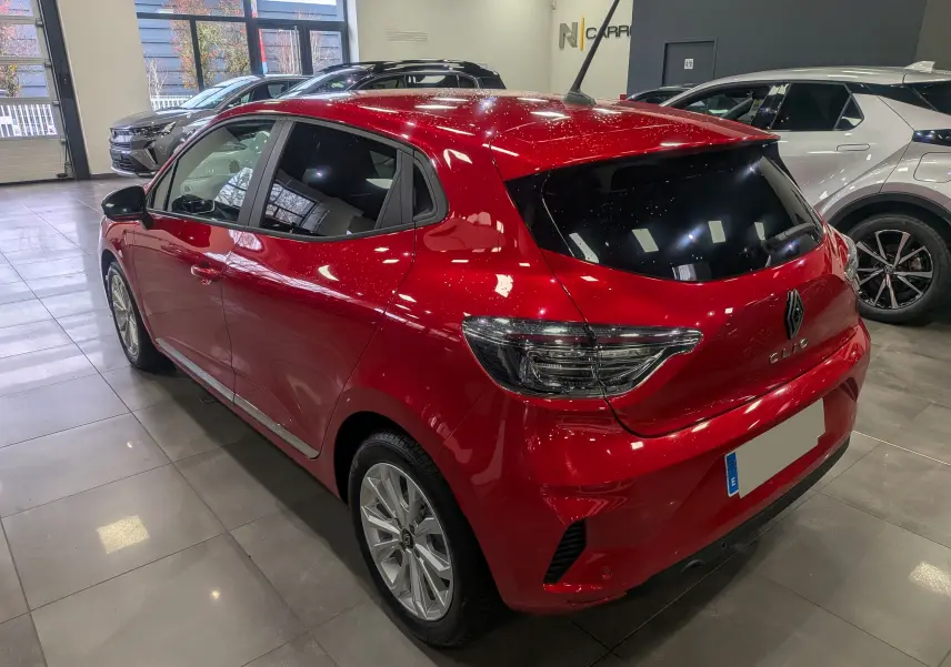 Vue 3/4 arrière droite d'une Renault Clio V Rouge Flamme en showroom, avec vitres teintées et jantes alliage.
