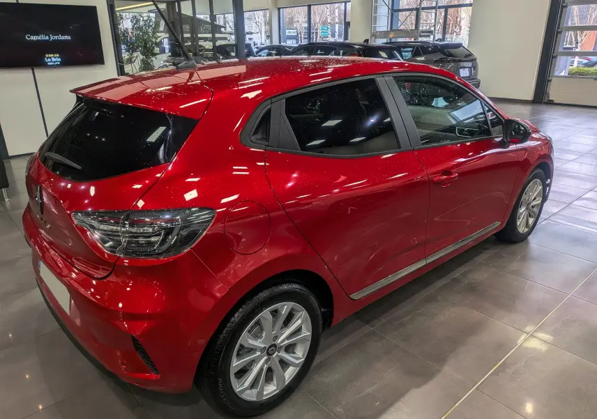 Vue 3/4 arrière droite d'une Renault Clio V Rouge Flamme en showroom, soulignant ses jantes alliage et vitres teintées.