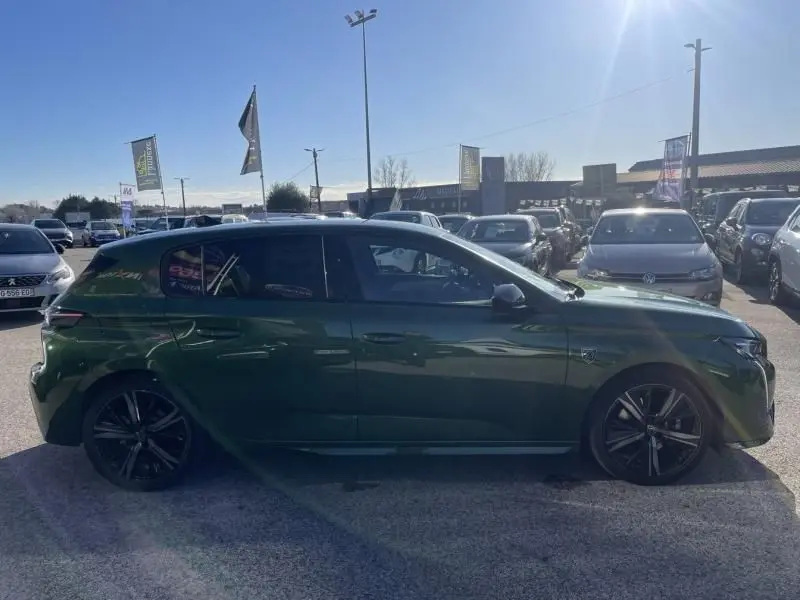 Vue de profil côté gauche d'une Peugeot 308 1.5 HDI 130 GT PACK 2022 en vert olivine avec jantes noires sur un parking.