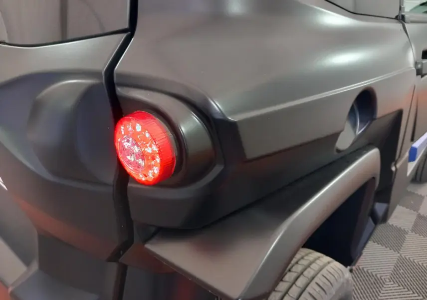 Gros plan sur le feu arrière droit rouge d’une Aixam Mega E-Scouty Evo bleu, soulignant ses lignes anguleuses.