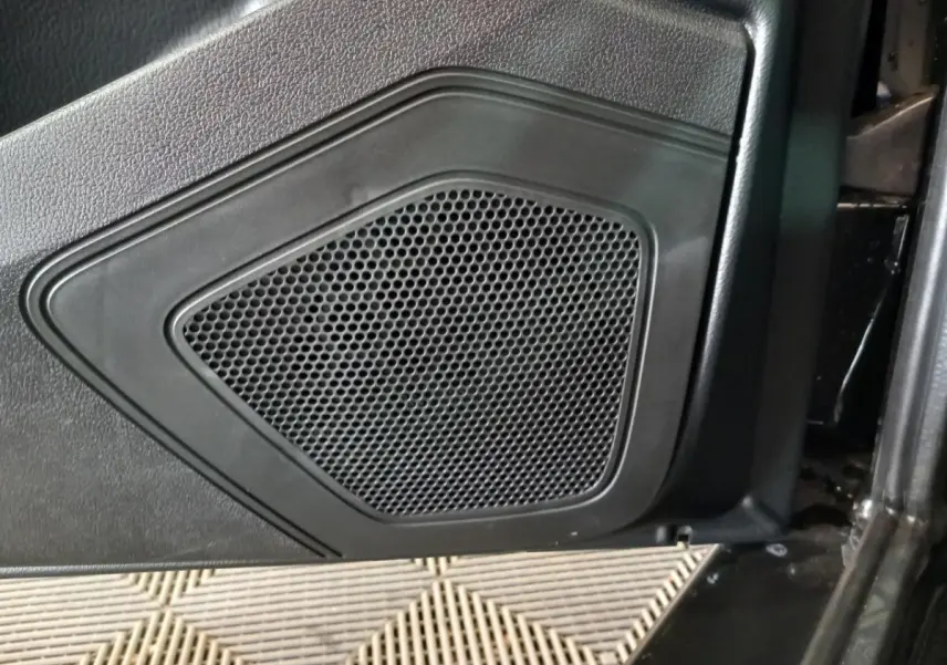 Gros plan sur la grille de haut-parleur intégrée à la porte intérieure noire d'un véhicule AIXAM MEGA bleu.