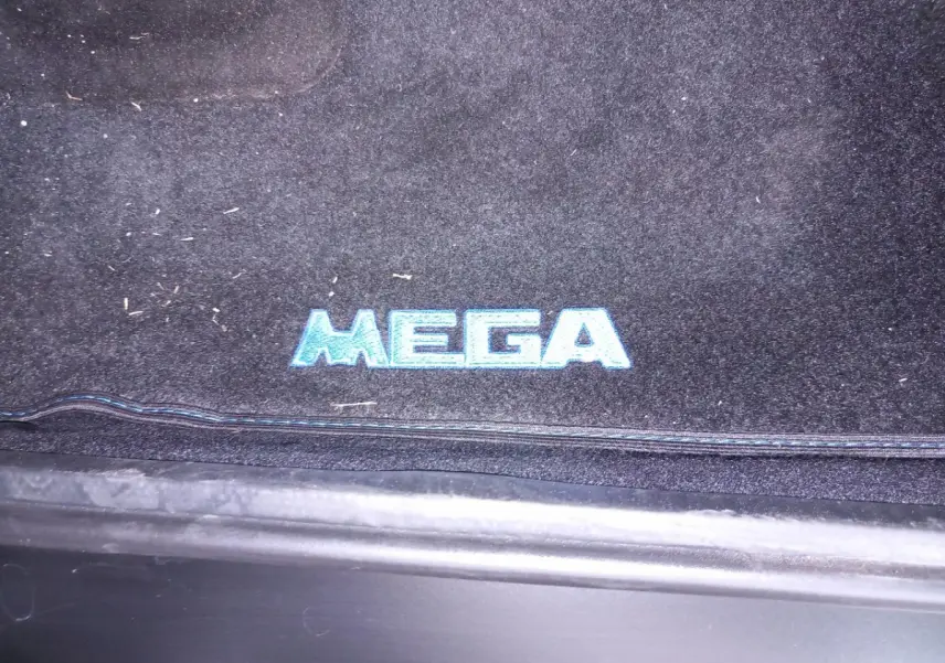 Gros plan sur le tapis de sol noir avec logo bleu "MEGA" à l'entrée côté conducteur d'un véhicule Aixam.