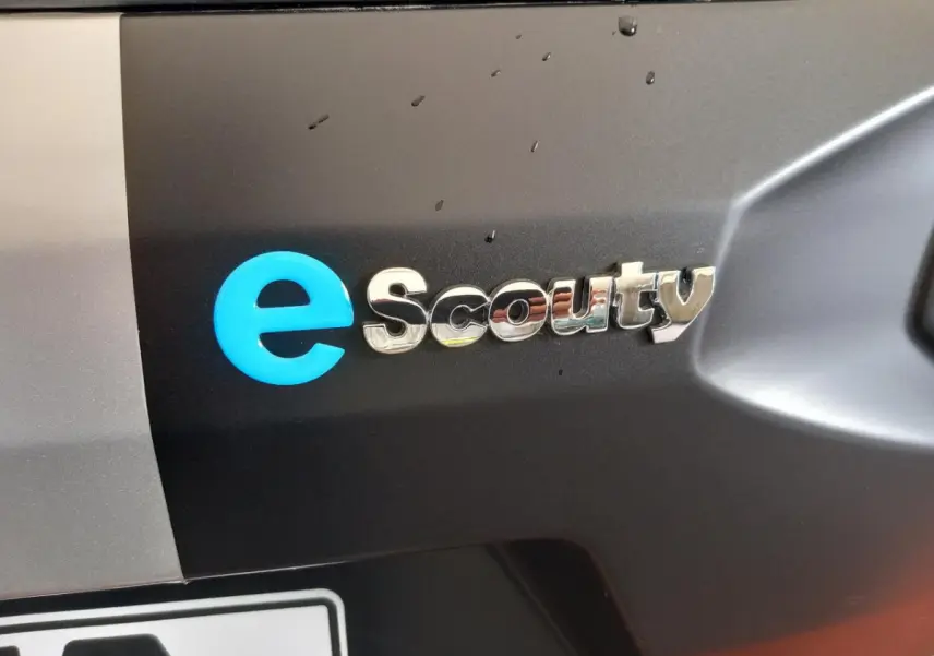 Gros plan sur le logo e-Scouty argenté et bleu sur la carrosserie noire d’un Aixam Mega électrique.