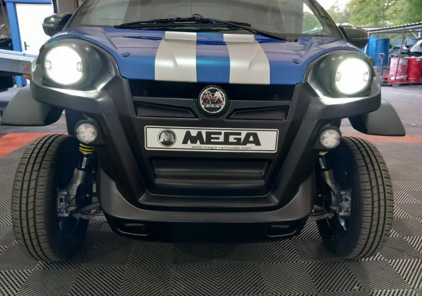 Vue frontale d'une Aixam MEGA E-Scouty Evo bleue avec phares allumés et bandes blanches sur le capot.