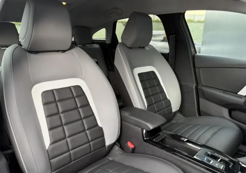 Vue intérieure des sièges avant gris clair et noir de la Citroën C4 Hybrid 2025 avec accoudoir central et console brillante.