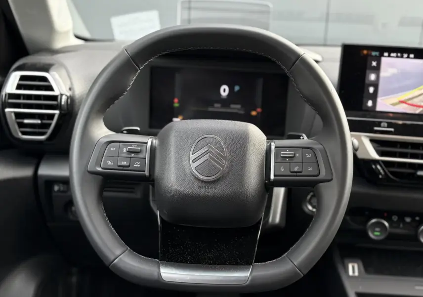 Vue rapprochée du volant cuir noir de la Citroën C4 2025 avec commandes intégrées et tableau de bord numérique en arrière-plan.
