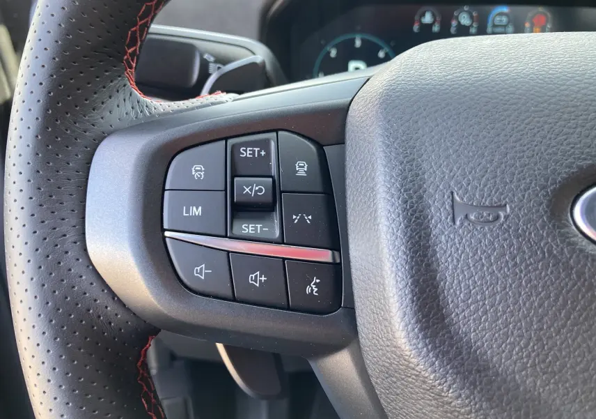 Gros plan sur les commandes à gauche du volant cuir perforé avec surpiqûres rouges du Ford Ranger Raptor gris commandeur.