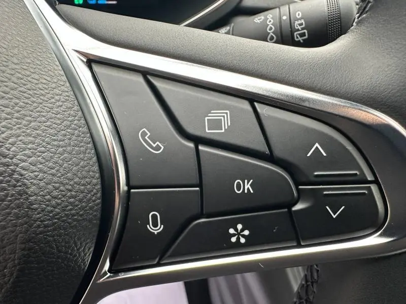 Gros plan sur les commandes multifonctions noires du volant du Renault Captur rouge, avec boutons de navigation et appel.