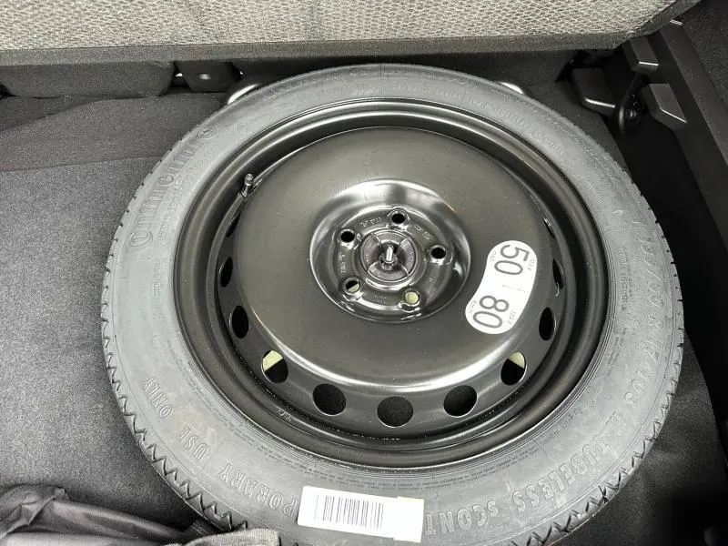 Gros plan sur la roue de secours noire dans le coffre du Renault Captur rouge 2025, visible sous la banquette arrière.