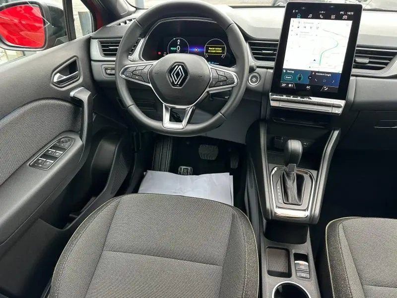 Vue intérieure avant du Renault Captur rouge 2025, volant multifonction, écran tactile vertical et levier de boîte auto.