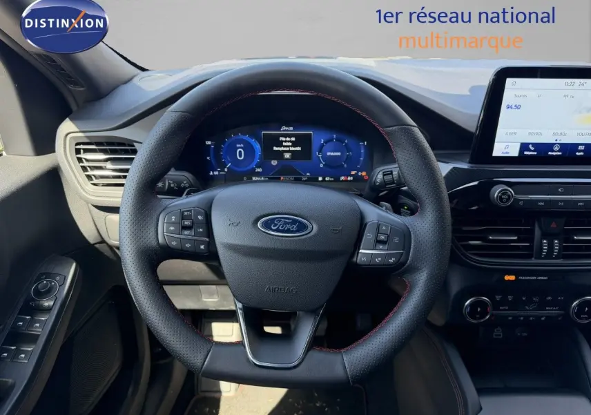 Vue intérieure centrée sur le volant cuir noir avec surpiqûres rouges du Ford Kuga 2024, tableau de bord digital et écran tactile.