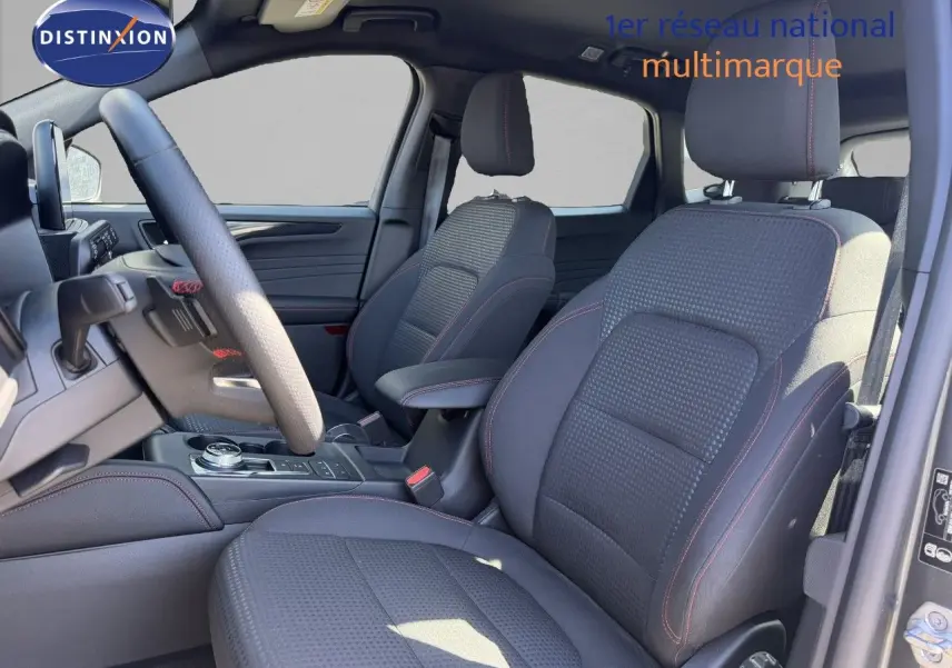 Vue intérieure côté conducteur du Ford Kuga 2024, sièges tissu noir avec surpiqûres rouges et volant multifonction.