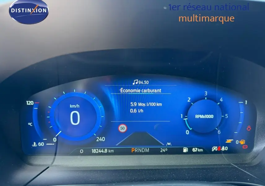 Vue rapprochée du tableau de bord numérique bleu du Ford Kuga 2024, affichant vitesse, régime et consommation.