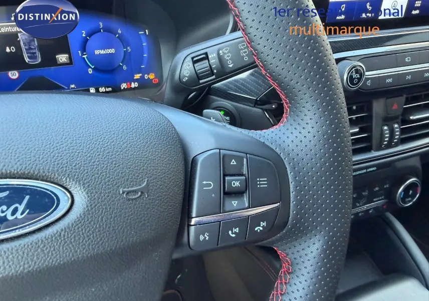 Vue rapprochée du volant en cuir perforé noir avec surpiqûres rouges du Ford Kuga 2024 gris magnétique, tableau de bord digital visible.