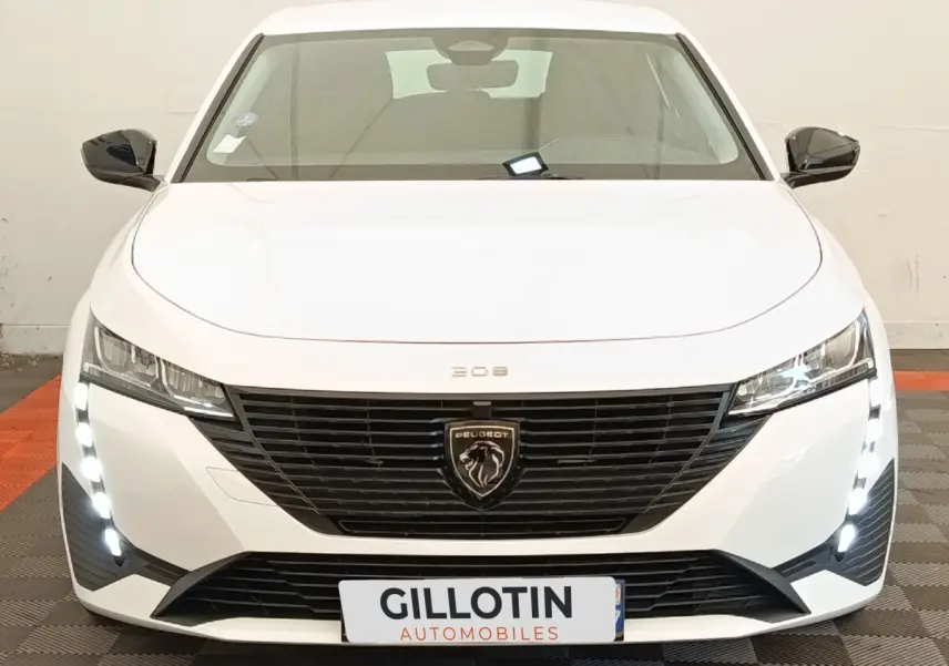 Vue frontale d'une Peugeot 308 blanche 2023 avec calandre noire et feux LED verticaux allumés.