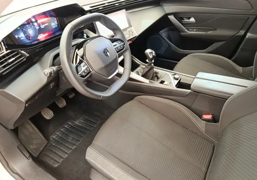 Vue intérieure côté conducteur de la Peugeot 308 PureTech 130 blanche, volant cuir et tableau de bord digital.