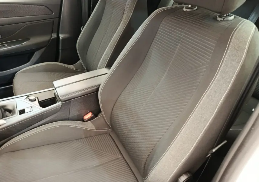 Gros plan sur les sièges avant gris foncé et la console centrale de la Peugeot 308 blanche, version 2023.