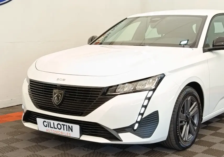 Peugeot 308 blanc vue 3/4 avant droit, avec calandre noire et feux LED verticaux distinctifs.
