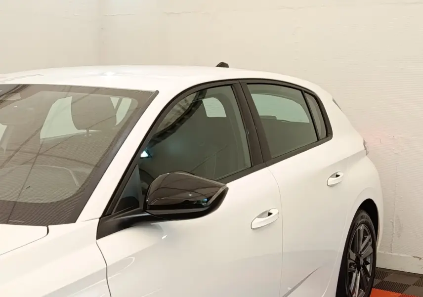 Vue côté gauche d'une Peugeot 308 blanche 2023 avec rétroviseur noir brillant et jantes alliage distinctives.