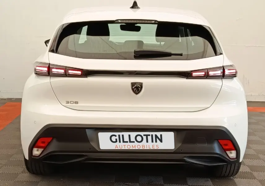 Vue arrière d'une Peugeot 308 blanche 2023 avec feux LED allumés et logo lion central sur le hayon.