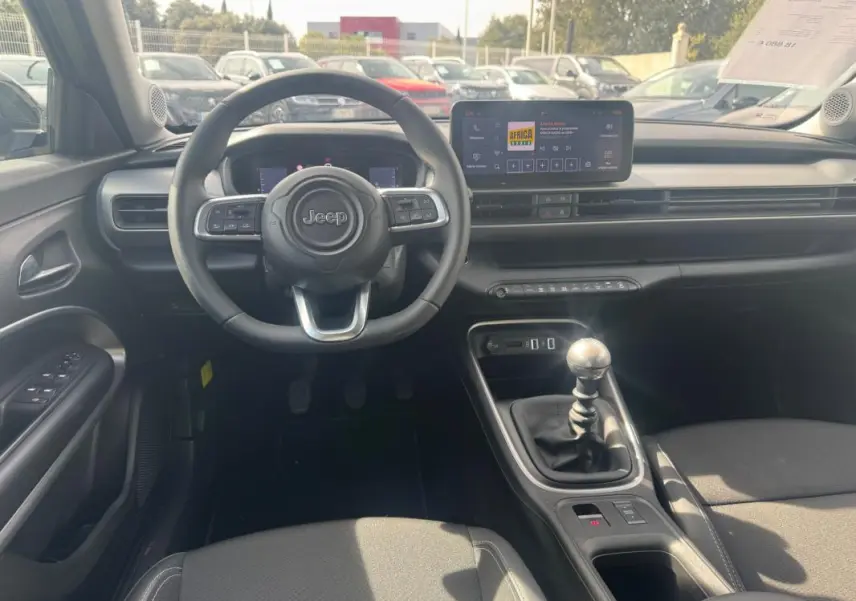 Intérieur du Jeep Avenger gris foncé vu de face, avec volant multifonction, écran tactile et levier de vitesses manuel.