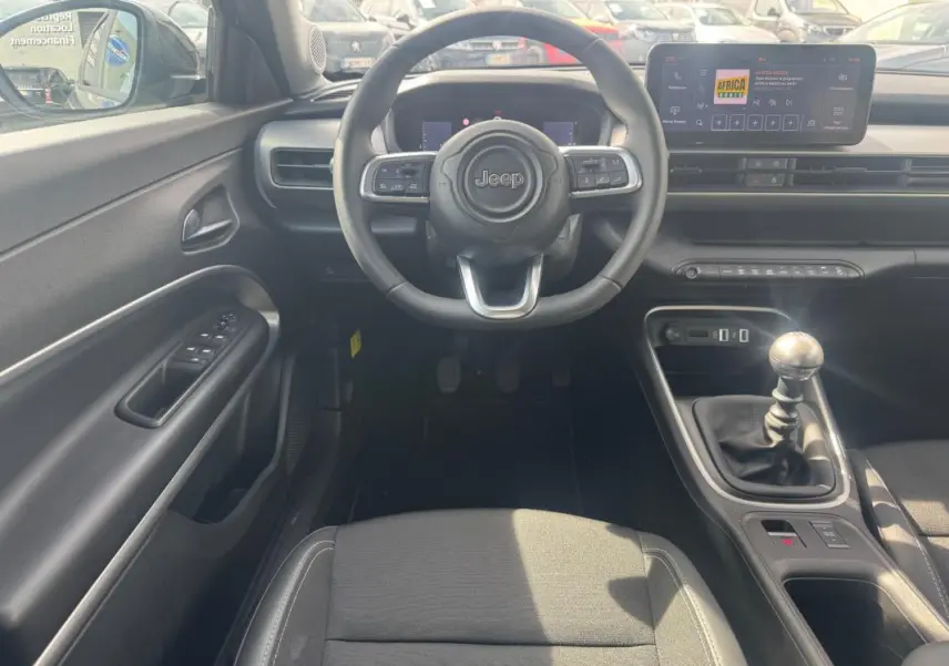 Vue intérieure frontale du Jeep Avenger 2025 gris foncé, volant multifonction et levier de vitesse manuel visibles.
