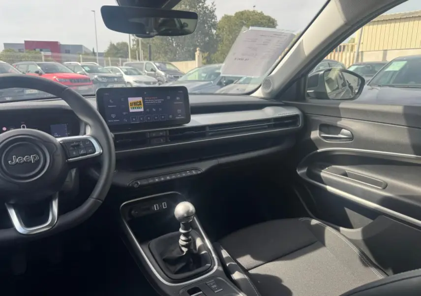 Intérieur du Jeep Avenger gris foncé vu côté conducteur, avec tableau de bord moderne et levier de vitesses manuel visible.