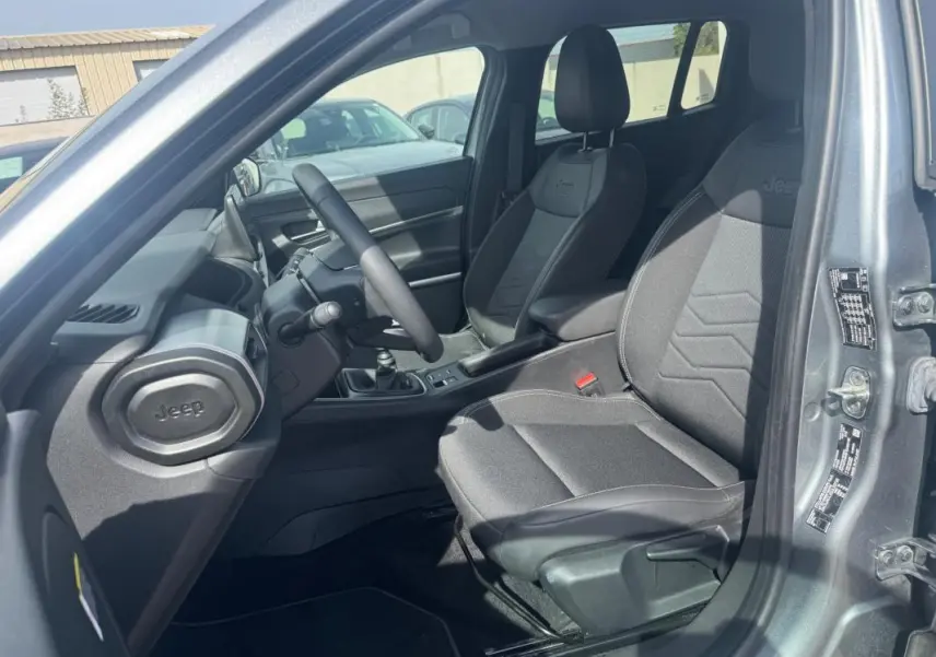 Vue intérieure côté conducteur du Jeep Avenger gris foncé 2025, montrant les sièges et la console avec boîte manuelle.