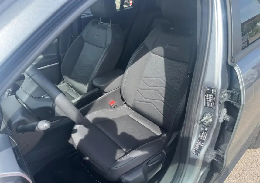 Vue intérieure côté conducteur du Jeep Avenger 2025 gris foncé, mettant en valeur les sièges noirs avec logo Jeep brodé.