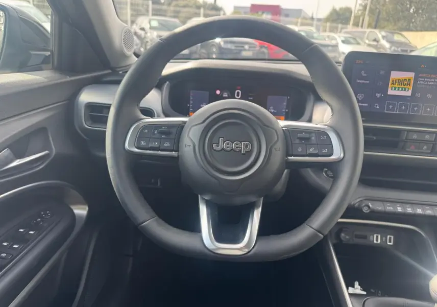 Vue intérieure centrée sur le volant Jeep noir du Jeep Avenger 2025, avec tableau de bord digital et écran tactile visible.