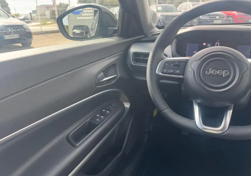 Vue intérieure côté conducteur du Jeep Avenger 2025 gris foncé, avec volant multifonctions et tableau de bord numérique.