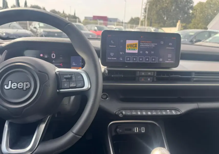 Vue intérieure de face du tableau de bord gris foncé du Jeep Avenger 2025 avec volant, écran tactile et levier de vitesse manuel.