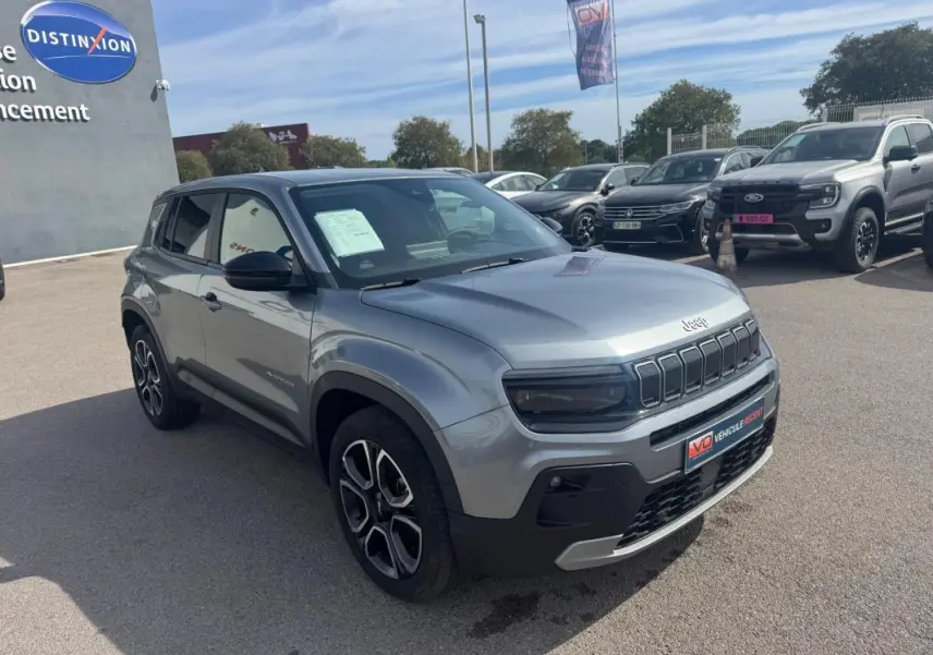 Jeep Avenger gris foncé vu en 3/4 avant droit sur parking, avec calandre distinctive et jantes noires et argentées.