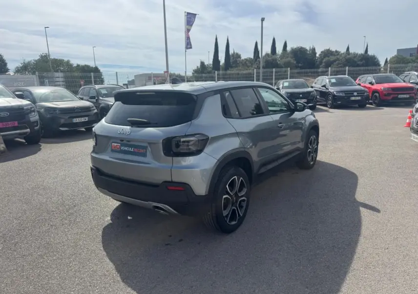Jeep Avenger gris foncé vu en 3/4 arrière droit sur un parking, avec feux arrière sombres et jantes distinctives.