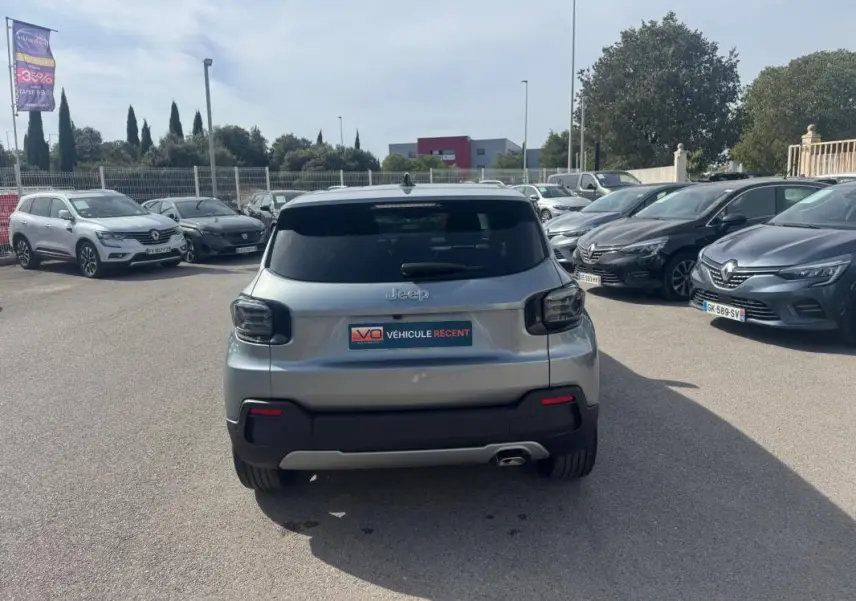 Vue arrière d'un Jeep Avenger gris foncé 2025, avec feux arrière fumés et plaque V.O. Véhicule récent visible en parking.