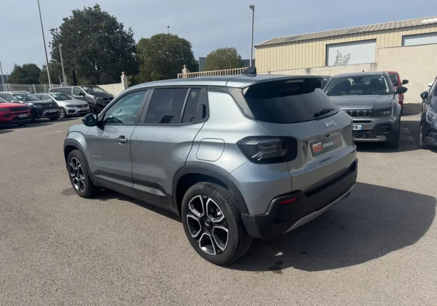 Jeep Avenger gris foncé vue 3/4 arrière droit, avec jantes spécifiques et vitres arrière teintées, stationné en extérieur.