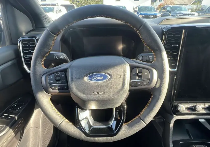 Vue rapprochée du volant cuir noir avec surpiqûres marron du Ford Ranger 2026, tableau de bord et écran tactile visibles.