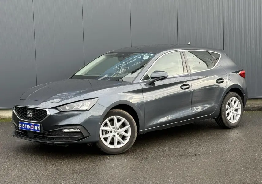 SEAT Leon 1.5 TSI 115 Style gris magnétique en 3/4 avant droit, jantes alliage 16 pouces visibles, stationnée sur sol humide.