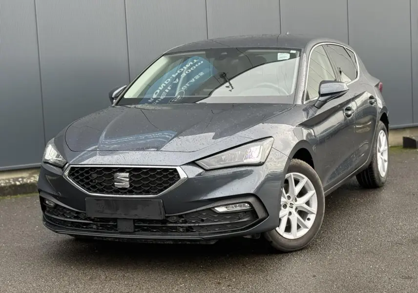 SEAT Leon 1.5 TSI gris magnétique vue 3/4 avant droit avec jantes alliage blanches sur sol humide.