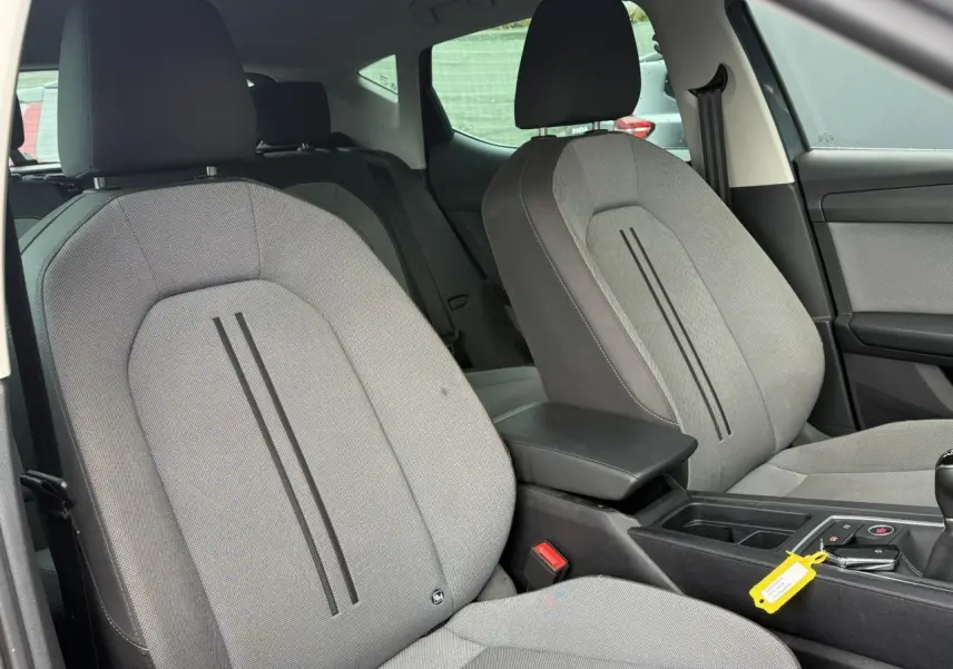 Vue intérieure côté avant droit du SEAT LEON 1.5 TSI 115 Style 2025 avec sièges tissu gris clair et accoudoir central noir.