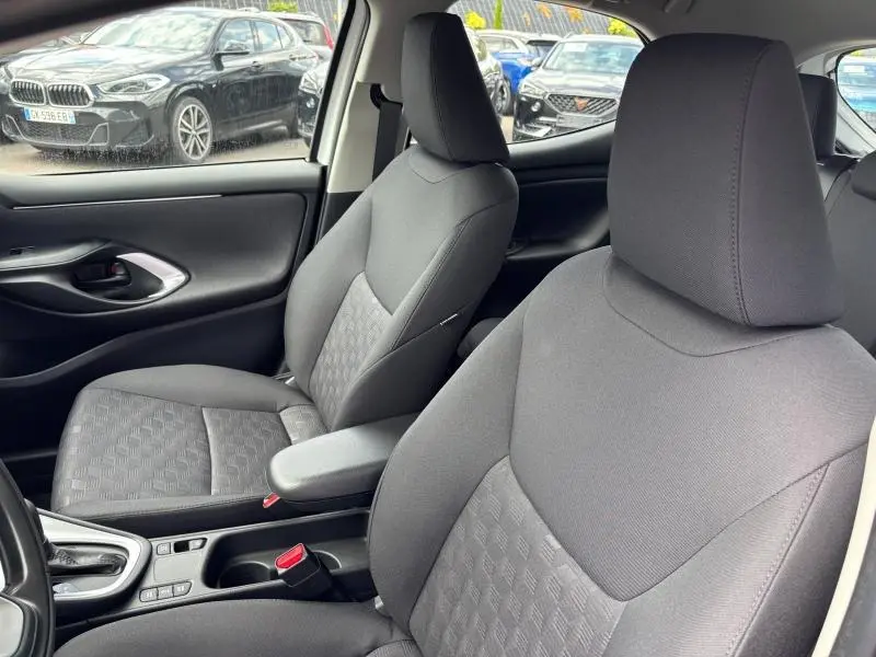 Vue intérieure des sièges avant en tissu gris de la Toyota Yaris 116h Dynamic 2025 avec accoudoir central et console.