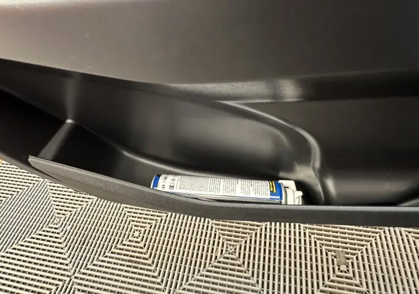 Gros plan sur le rangement intérieur noir d'une Aixam Ambition 0.5 City Pack blanc, avec une bombe aérosol posée.