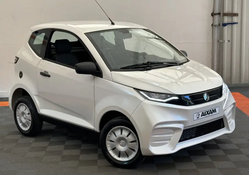 Vue 3/4 avant d'une Aixam Ambition 0.5 City Pack blanche avec rétroviseur caméra côté gauche visible.