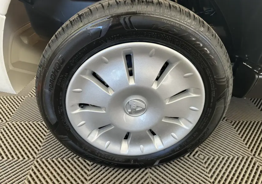 Gros plan sur la roue avant droite d'une Aixam Ambition blanche, avec enjoliveur argenté et logo central visible.