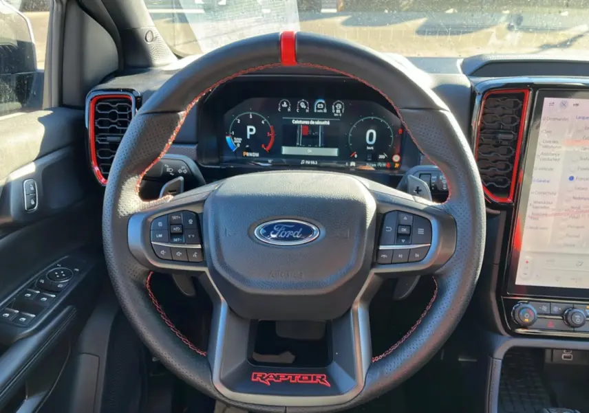 Vue intérieure centrée sur le volant cuir noir avec surpiqûres rouges et logo Raptor rouge du Ford Ranger 2025.
